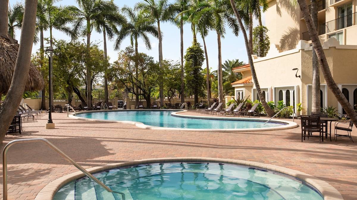 Stone pool deck with a hot tub and pool surrounded by tropical foliage